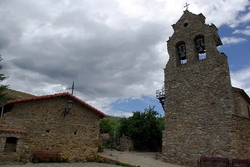 Steinerner Kirchturm in Valdesamario mit wolkigem Himmel.
