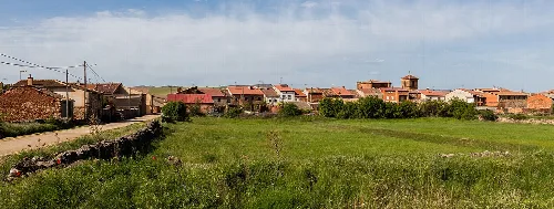 Blick auf ein Dorf mit Häusern und grünem Feld im Vordergrund.