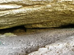 Inside a cave with rock layers and a dirt and stone floor.