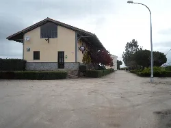 Two-story building with a gabled roof and small windows, next to a road and trees.