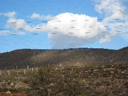 Paneles fotovoltaicos en una ladera de montaña con cielo azul y nubes.