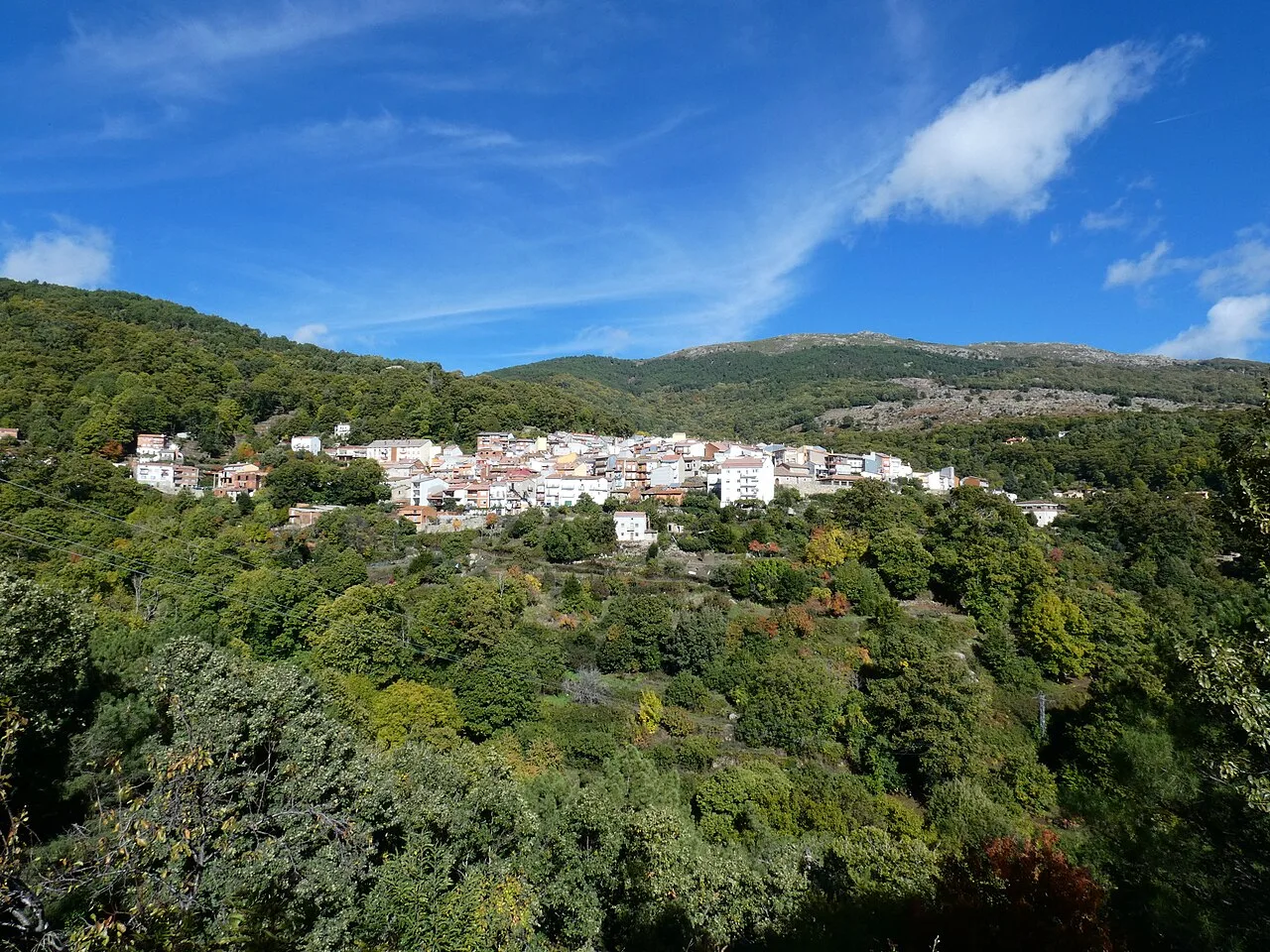 Pueblo de Casillas en una ladera con árboles y montañas al fondo.