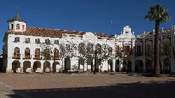 Rathaus mit Bögen und Bäumen im Platz.