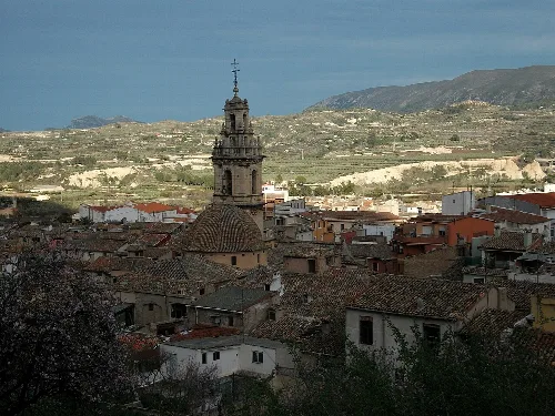 Vista de Cocentaina con iglesia y casas tradicionales, montañas al fondo.