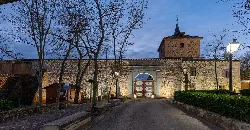 Entrada a la plaza de toros cuadrada con árboles y farolas en Santa Cruz de Mudela.