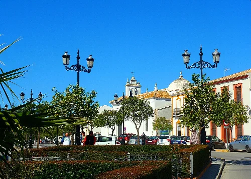 Stadplatz in Hinojos mit Bäumen, Laternen und traditionellen Gebäuden.