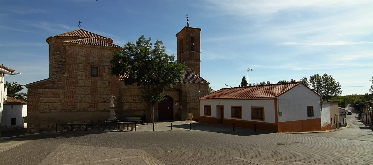 Square with stone church and white building in Arcicóllar.