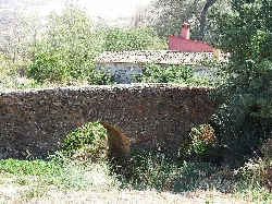 Stone bridge with an arch in Garcíaz, surrounded by trees and vegetation.