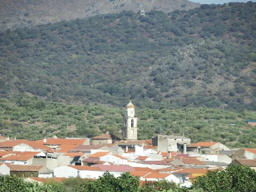Blick auf eine Stadt mit Kirche und roten Dächern in einer grünen Hügelregion.
