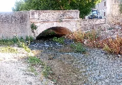 Stone bridge over a stream with vegetation and flowing water.