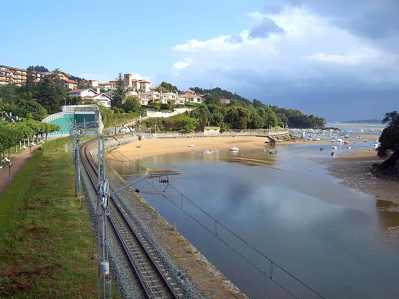 Blick auf den Toña-Strand in Sukarrieta mit Meer, Booten und Häusern auf dem Hügel.