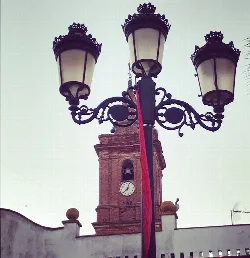 Church tower of Alosno with clock and iron street lamp in foreground.