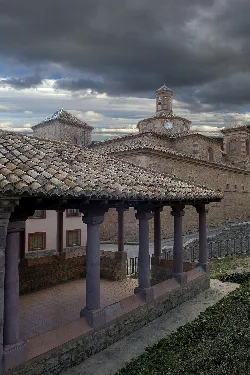 Tile roof and columns of a porch in the foreground, with the church and cloudy sky in the background.