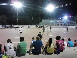 Players and spectators on a futsal court lit up at night.
