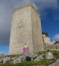 Large square stone tower in Estepa, Seville, with signage in the foreground.