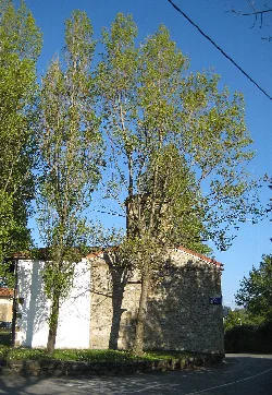 Pequeña ermita de Santa Ana con árboles y una calle en Berango.