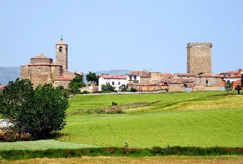 Grüne Felder und Gebäude mit Türmen in Noviercas, Soria.