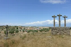 Three stone crosses in a field with trees and a village in the background.
