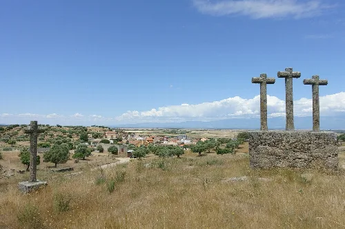 Drei Steinkreuze in einem Feld mit Bäumen und einem Dorf im Hintergrund.