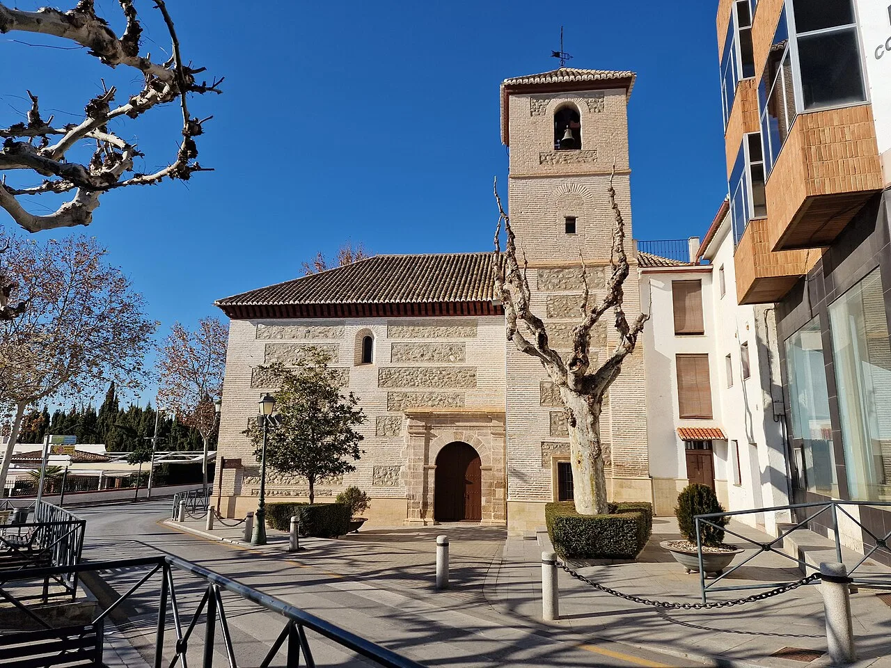 Kirche der Inkarnation in Huétor Vega mit Bäumen und modernem Gebäude.