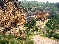 Camino de tierra junto a acantilados con pinturas rupestres en la roca.
