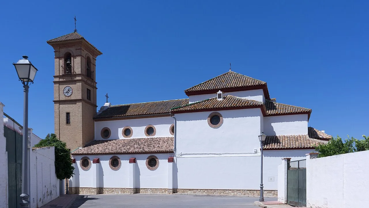 Weiße Kirche mit Turm und Wänden in Humilladero, Málaga, unter blauem Himmel.