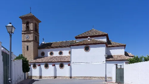 Weiße Kirche mit Turm und Wänden in Humilladero, Málaga, unter blauem Himmel.