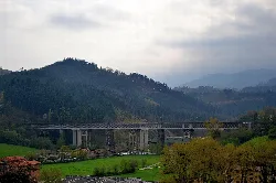 Bridge of Ormaiztegi over a valley with mountains and cloudy sky.