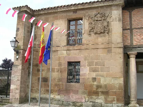 Fachada de piedra con escudo y banderas en la plaza de Cartes.