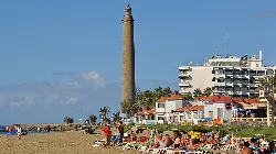 Faro alto junto a edificios y gente en la playa.