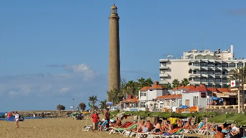Hoher Leuchtturm neben Gebäuden und Menschen am Strand.