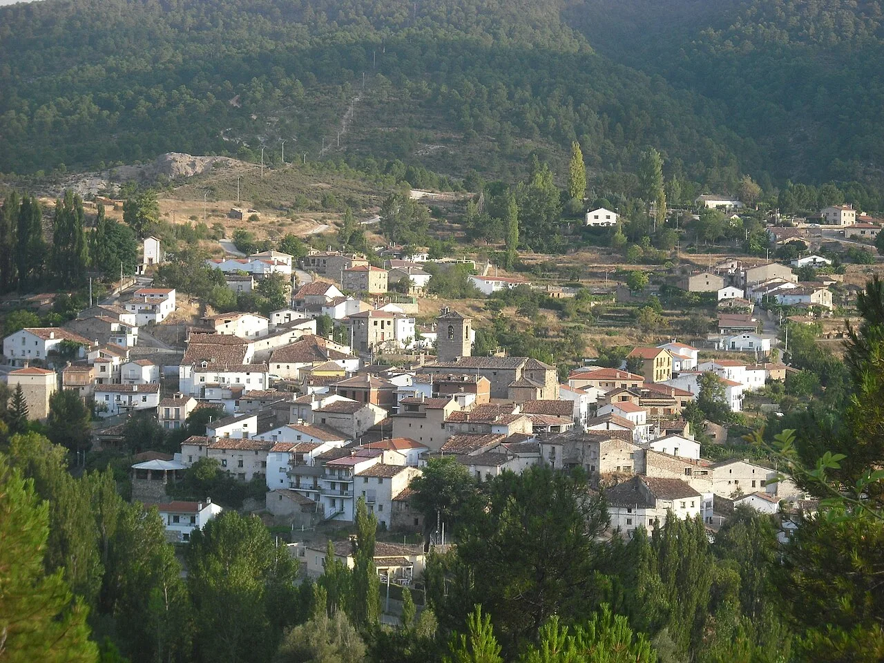 Vista de Fuertescusa con casas blancas y verdes en un valle rodeado de montañas.