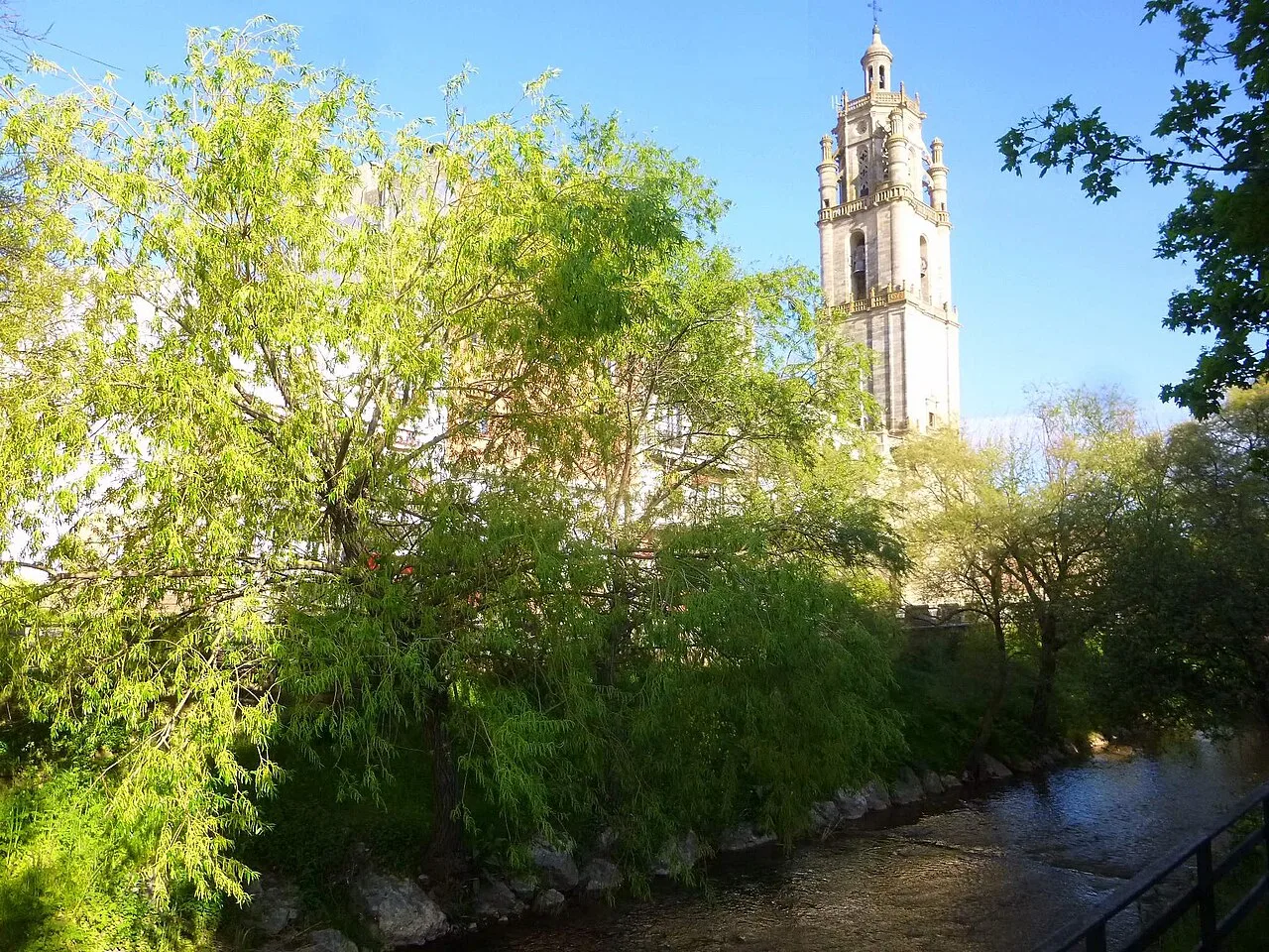 Santa María Church and the Odrón River in Los Arcos, Navarra, with green trees.