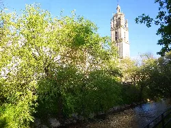 Santa María Church and the Odrón River in Los Arcos, Navarra, with green trees.