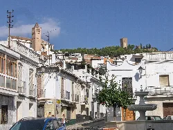 Calles de Vélez-Málaga con casas blancas y un castillo en la colina.