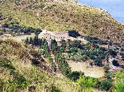 Pequeña ermita en una colina con vegetación y vista al mar.