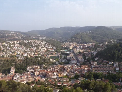 Panoramablick auf Vallirana vom Mirador, mit Häusern und Straßen in einem Tal, umgeben von Hügeln.