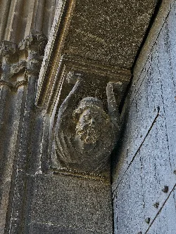 Sculpture of a bearded face with raised arms on the church portal.