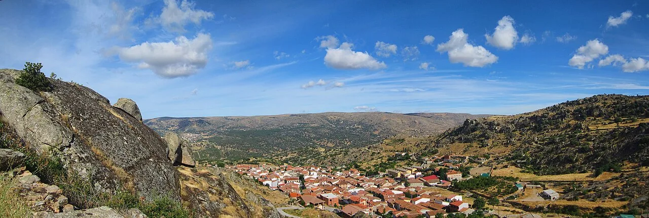 Panoramablick auf San Bartolomé de Pinares mit Häusern und Hügeln unter einem blauen Himmel.