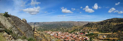 Panoramablick auf San Bartolomé de Pinares mit Häusern und Hügeln unter einem blauen Himmel.