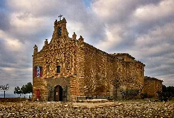 Stone church with decorated facade and a tree in front.
