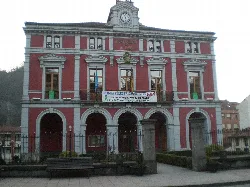 Edificio con fachada roja, reloj y arcos en la entrada en Aller, Asturias.
