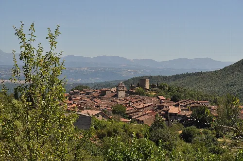 Blick auf eine Stadt mit Ziegeldächern und Bergen im Hintergrund.