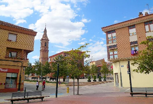 Platz mit Bäumen, Bänken und Kirchturm in Pradejón.