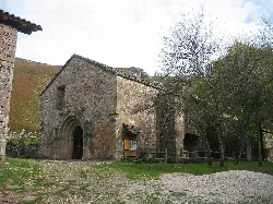 Iglesia antigua de piedra en un entorno rural con árboles y camino de grava.