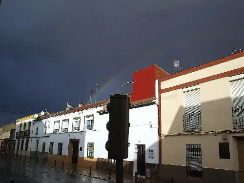 Streets with white houses and a rainbow in the cloudy sky.