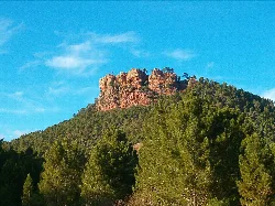 Cima de roca en un paisaje con árboles y cielo azul.