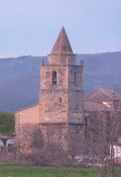 Torre de iglesia de piedra con un burro en primer plano al atardecer.