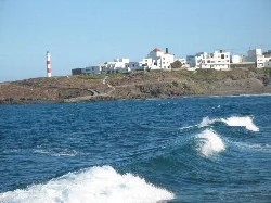 Lighthouse and white houses along the coast of Arico, Tenerife, with waves in the foreground.