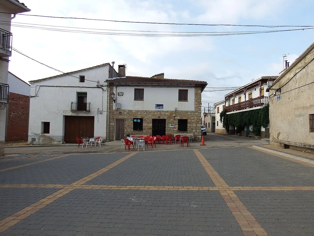 Platz mit roten Tischen und Stühlen vor einem weißen und steinernen Gebäude in Campillos-Sierra.